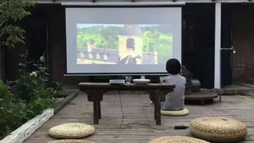 Una persona sentada en un taburete tejido frente a una pantalla de proyector que muestra un paisaje.