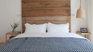 A bedroom with a wooden headboard, a checkered bedspread, a bedside table with a vase of flowers, and a hanging light fixture. - Beijing Migrator Mountain Resort (Changping)