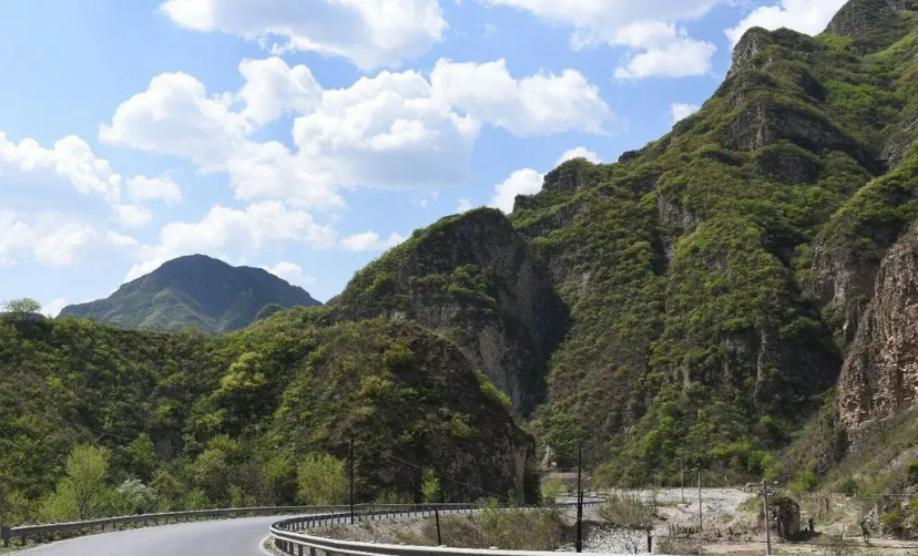 A winding road through a mountainous area with lush greenery and rocky cliffs.