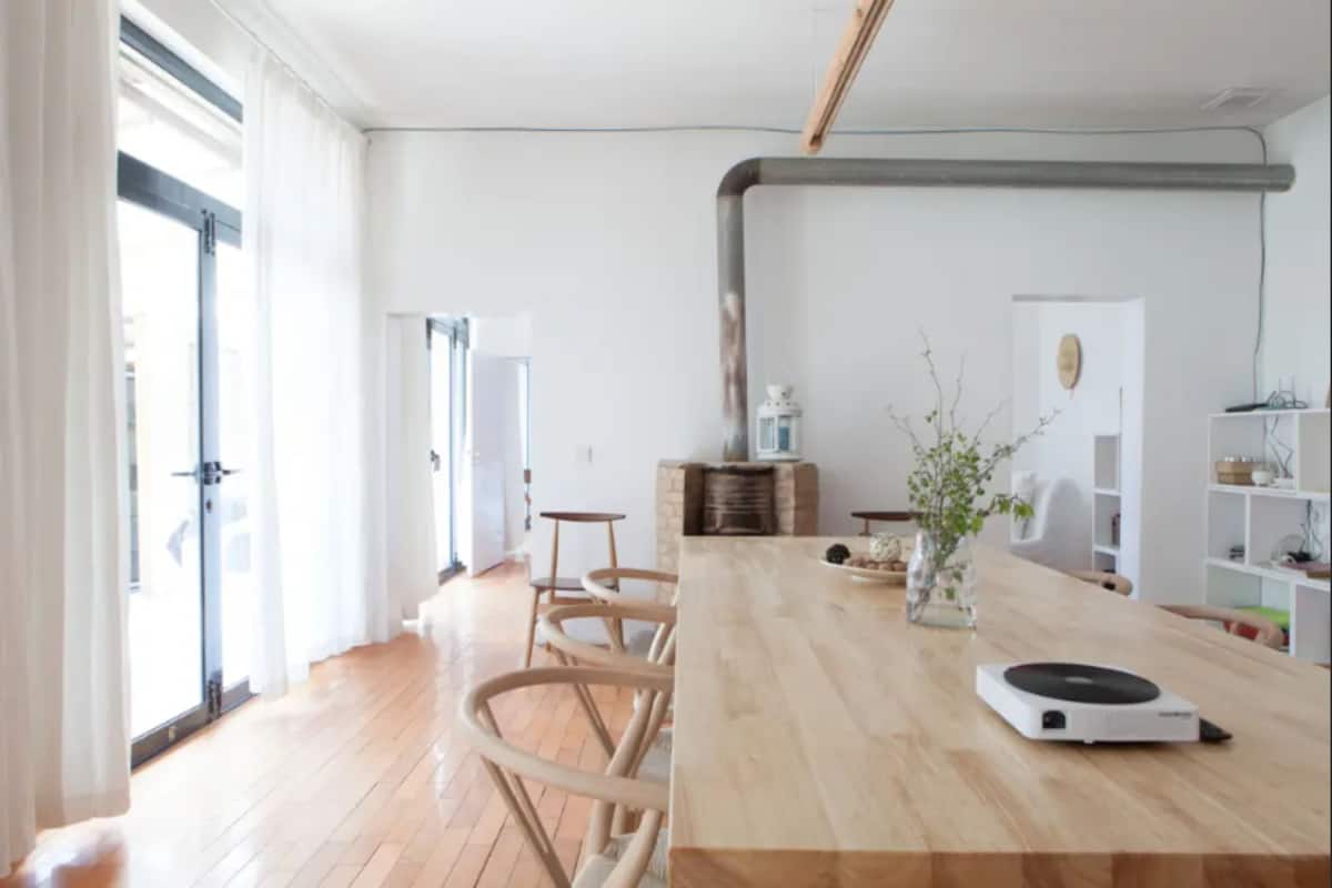 Una sala de estar moderna con una mesa de madera, una mesita de centro y una planta pequeña. Se observa una chimenea y una estantería al fondo.