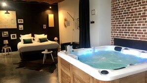 Quarto de hotel moderno com uma cama grande, uma banheira de hidromassagem de madeira e uma parede de tijolos.