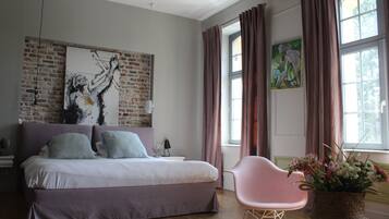 A bedroom with a bed, a chair, a window with curtains, and artwork on the walls.