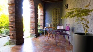 Um pátio externo com arcos de tijolo, piso de azulejos, uma mesa com cadeiras e um vaso de planta.