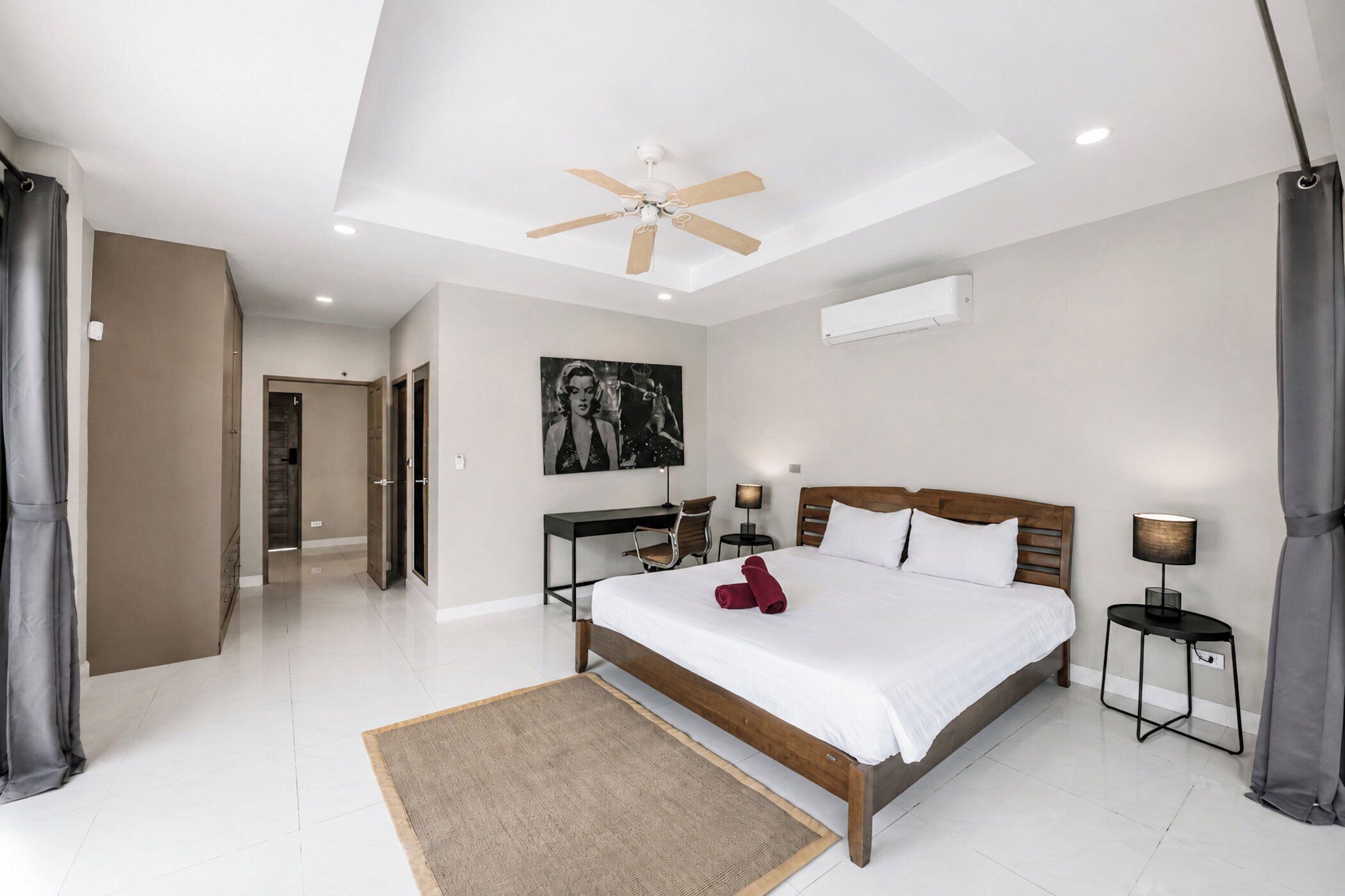Un dormitorio moderno con cama, mesitas de noche, ventilador de techo y un cuadro grande en la pared.