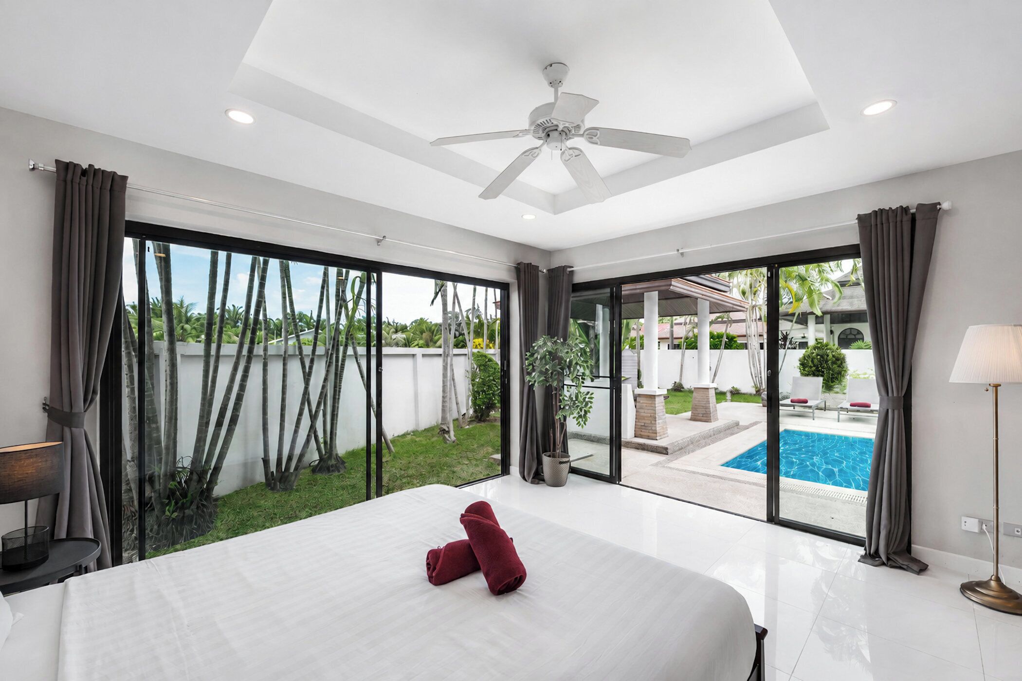Un dormitorio espacioso con una cama grande, un ventilador de techo y vista a una piscina a través de amplios ventanales correderas.