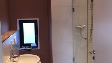 A bathroom with a glass-enclosed shower, a white sink, and patterned floor tiles.