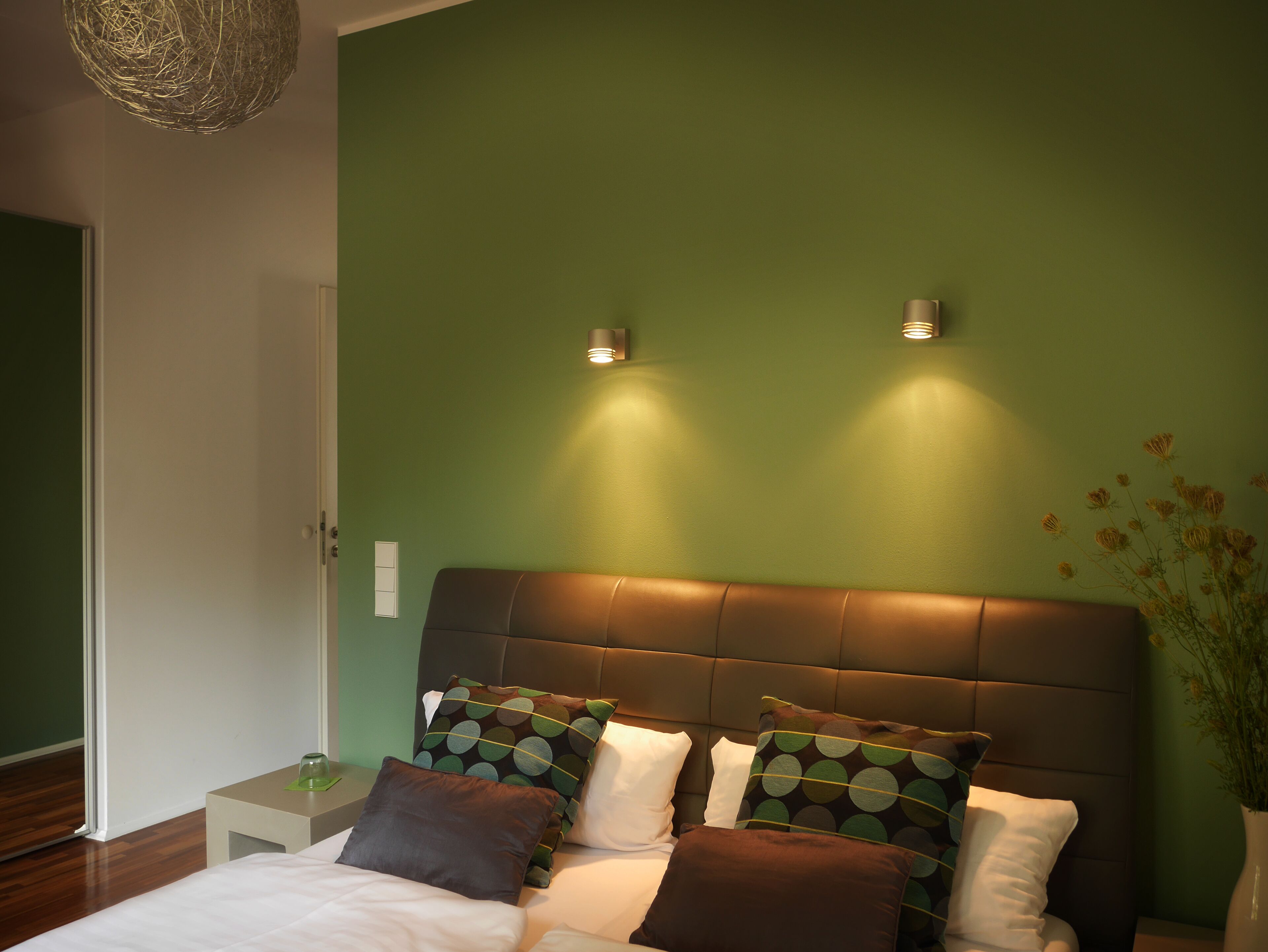 A bedroom with a green wall, a brown headboard, and two bedside lamps.
