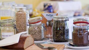 A variety of glass jars containing different grains and seeds, a loaf of bread, and a knife on a table.