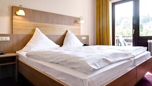 Une chambre d’hôtel avec une tête de lit en bois, deux lampes de chevet, une grande fenêtre avec des rideaux et un lit soigneusement fait.