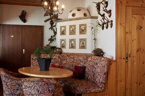 Ein gemütliches Zimmer mit einer Holztür, einem runden Tisch mit einem Topfpflanzen und einem floralen Sofa, sowie Wandbildern von Tierkopfskulpturen und Spiegeln.