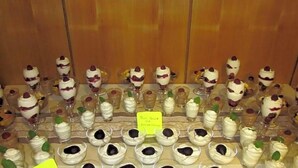 Diversas opciones de postres en una mesa, incluyendo postres en capas y porciones individuales en recipientes pequeños.