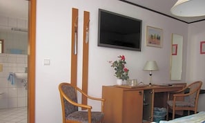 Una habitación de hotel con una cama, un escritorio con una silla, un televisor y una pequeña mesa con un florero.