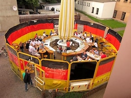 Un espacio exterior de comedor circular con varias mesas y sillas, rodeado por una barrera amarilla y roja.