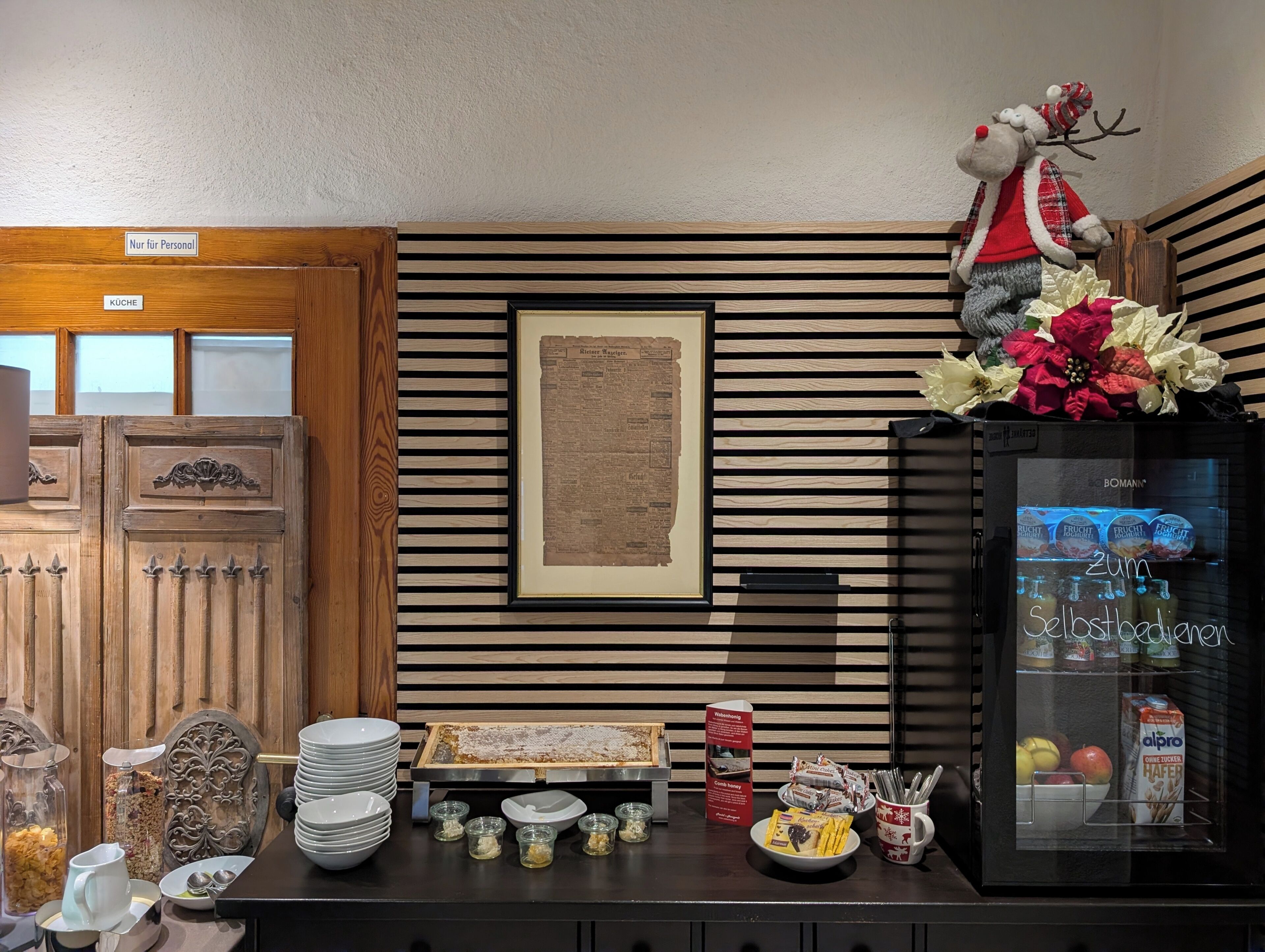A kitchenette with a refrigerator, a wooden cabinet, a framed menu, and various food items.