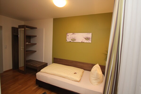 Quarto com cama, um banco de madeira, estante e um quadro na parede.