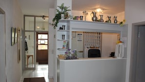 A reception desk with a white counter, a potted plant, and various decorative items. There is a door with a sign above it, and a chair is visible in the background. - Hotel-Gasthof Weißes Roß (Kleinostheim)