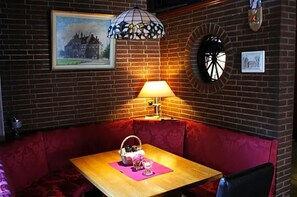 A cozy corner with a wooden table, a red cushioned bench, a wall-mounted lamp, and a framed picture.