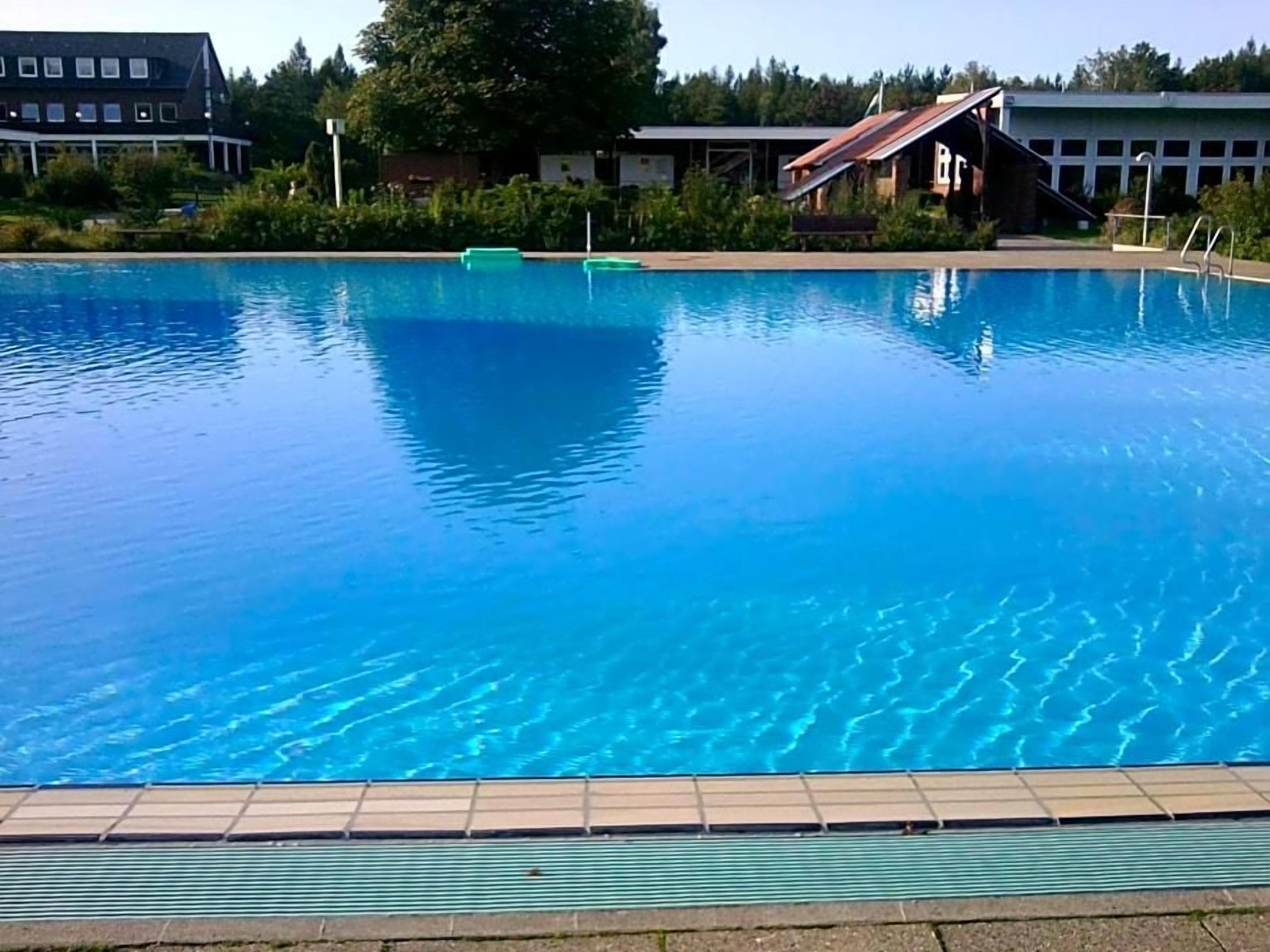 Een zwembad met helderblauw water, omringd door gebouwen en groen.