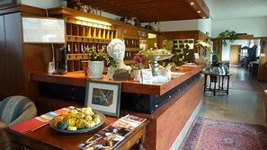 A reception area with a counter, a bust sculpture, a coffee machine, and a bowl of fruit.