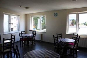 Una habitación con una mesa de comedor y sillas, ventanas amplias y un reloj en la pared.