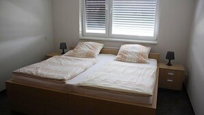 A double bed with a wooden frame, two bedside tables with lamps, and a window with blinds. - Hotel Grand Tour (Wesseling)