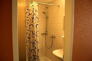 A shower with a patterned curtain, a handheld showerhead, and a wall-mounted faucet.