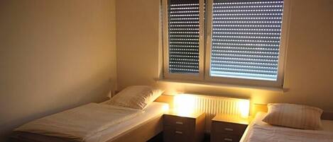 A bedroom with two single beds, a nightstand, and a window with blinds.