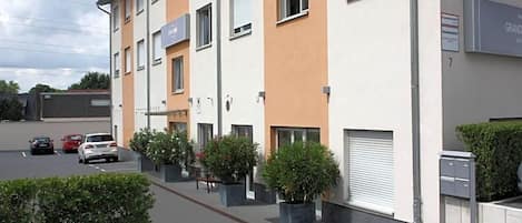 A multi-story residential building with a modern design, featuring balconies and a parking area with cars.