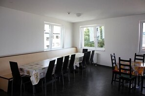 A room with a long table and chairs, large windows, and a radiator.