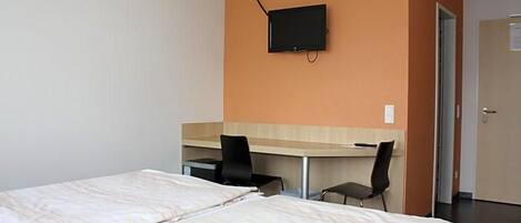 A hotel room with two beds, a desk, a chair, and a television mounted on the wall.