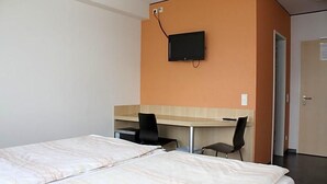 A hotel room with two beds, a desk, a chair, and a television mounted on the wall. - Hotel Grand Tour (Wesseling)