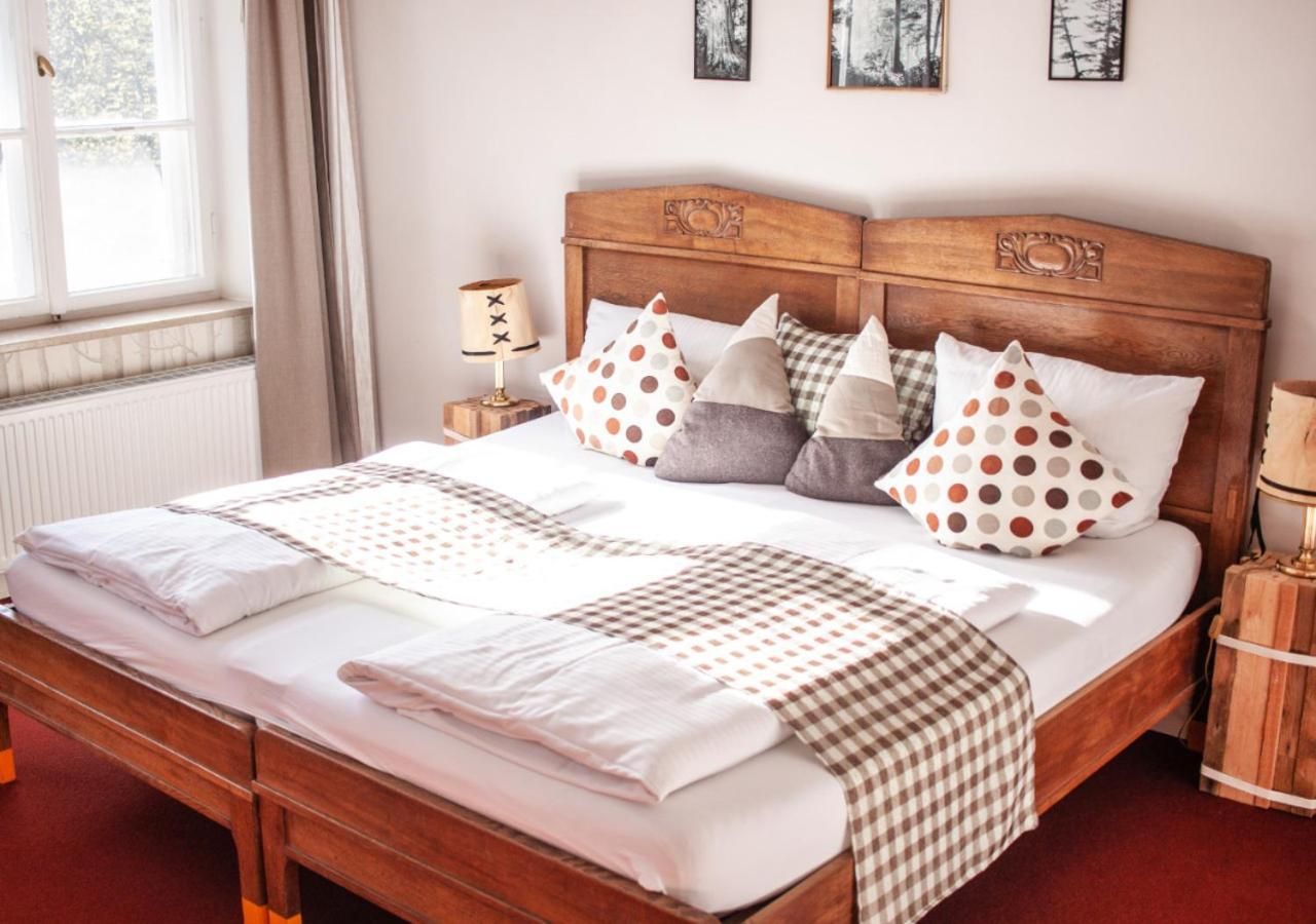 Un lit bien fait, avec une tête de lit en bois, plusieurs oreillers et une table de chevet sur laquelle se trouve une lampe.