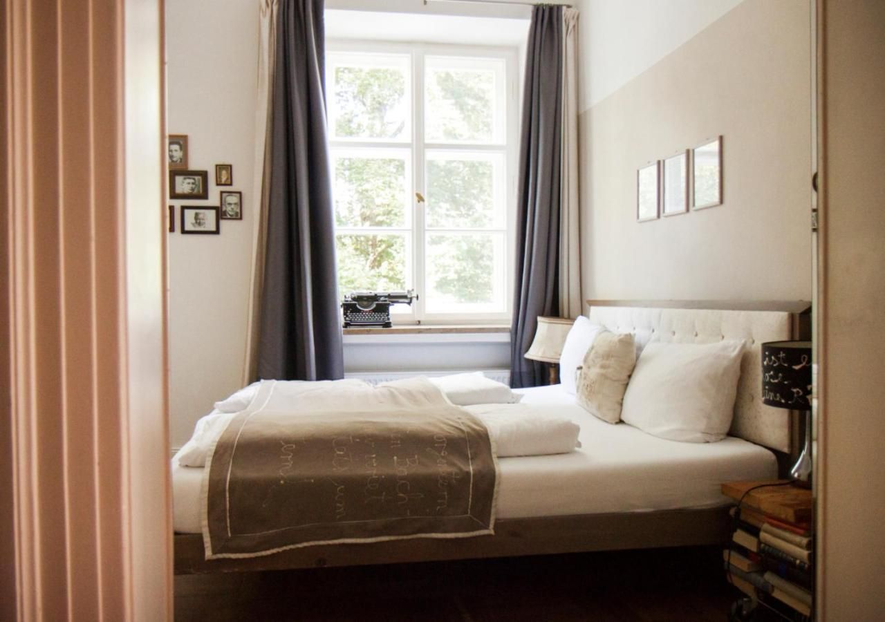 A bedroom with a bed, a window with curtains, a bedside lamp, and a wall with framed pictures.