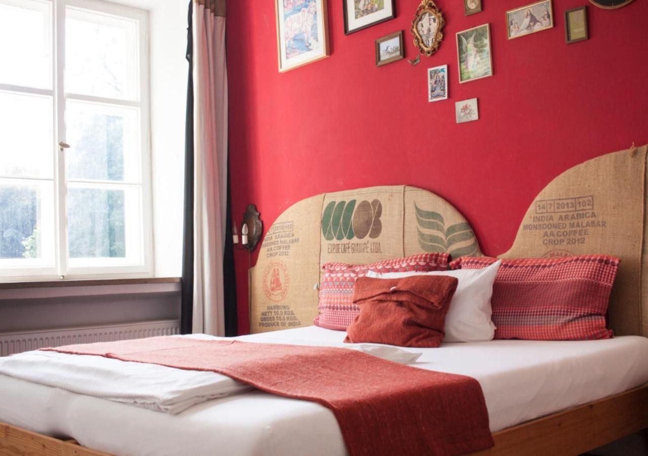 Una cama con una manta roja, almohadas y una pared con cuadros.