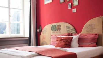 A bed with a red blanket, pillows, and a wall with framed pictures.