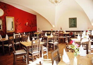 A restaurant with multiple tables and chairs, a red wall with a floral pattern, and a chandelier.