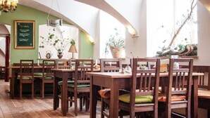 A restaurant with wooden tables and chairs, green walls, and a chandelier. - Hotel Schloss Blumenthal (Aichach)