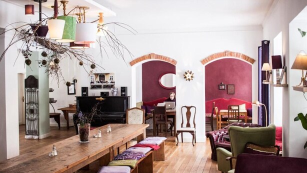 A spacious living room with a wooden dining table, comfortable seating, and a television. - Hotel Schloss Blumenthal (Aichach)