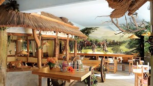 A rustic interior with wooden furniture, a stone fireplace, and a mural depicting a rural scene. - Kelten-Hotel (Unterbreizbach)
