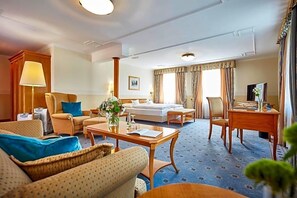 A hotel room with a sofa, armchair, dining table, and a television.