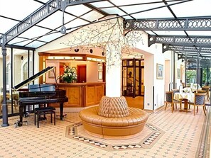 A grand lobby with a piano, a round seating area, and a glass ceiling structure.