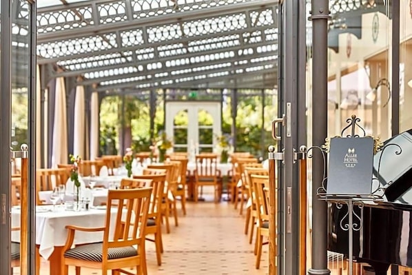 An outdoor dining area with wooden tables and chairs, a piano, and a sign for the Allée Hotel.