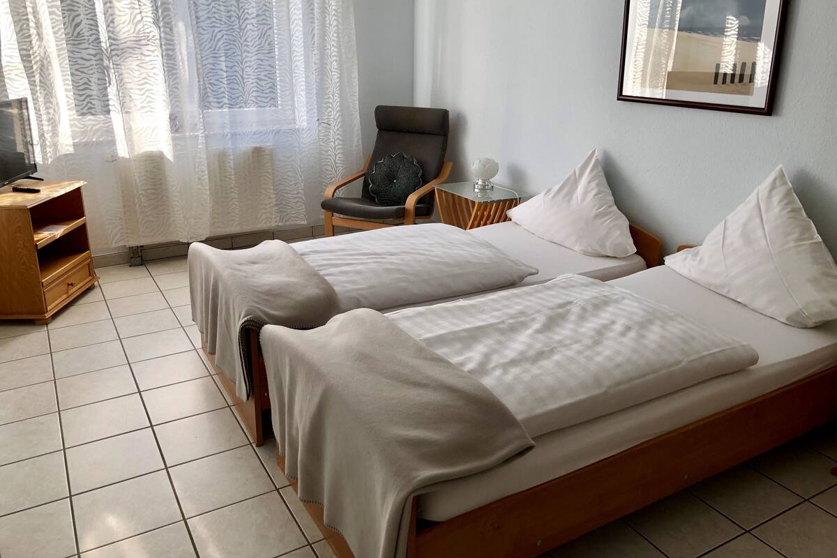 A hotel room with two beds, a chair, a small table, and a framed picture on the wall.