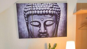 Un salon moderne avec un téléviseur à écran plat, une œuvre d’art représentant un Bouddha accrochée au mur, une petite plante et une lampe de chevet.