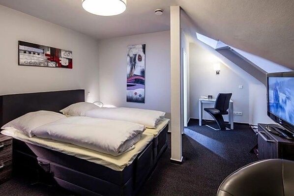 A modern hotel room with two beds, a desk, a chair, and a television.