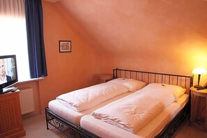 A room with two single beds, a television on a wooden cabinet, a small table with a lamp, and a window with curtains.
