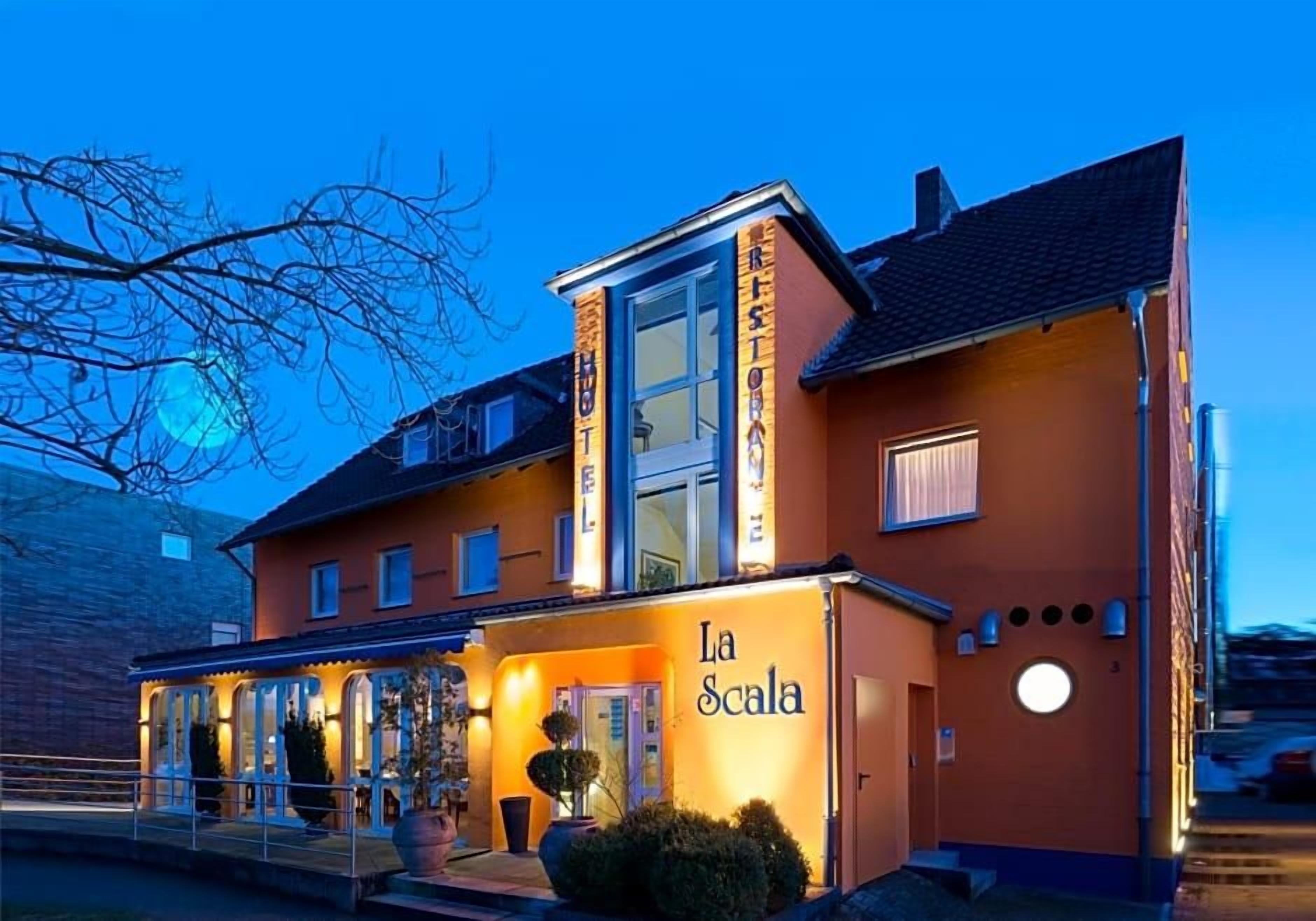 Un hotel con un ingresso ben visibile, una zona esterna coperta e una facciata luminosa.