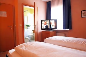 Una habitación de hotel con una cama, un televisor sobre un mueble y una puerta que da a un baño.