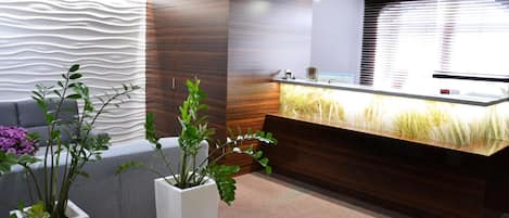 A reception area with a modern design, including a reception desk, a sofa, and potted plants.