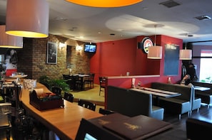 A restaurant interior with brick walls, a TV mounted on the wall, and a red accent wall.